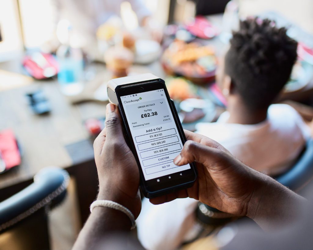 A waiter holds a TISSLPay Pay at Table card machine that provides embedded EPOS payments