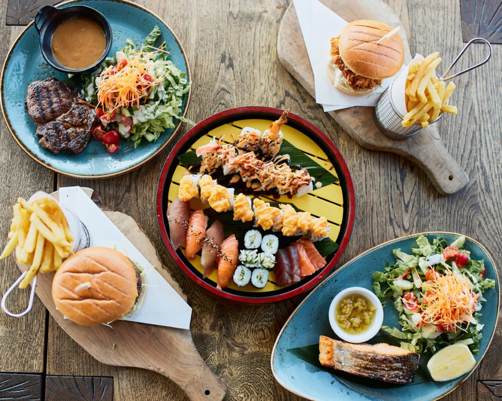 shot from above, a table holds a variety of menu items including salmon, sushi, and burger